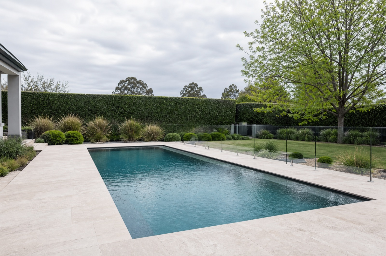 Modern pool framed by pale concrete paving and clipped hedging
